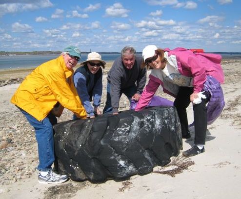 Four adults picking up large tire on beach